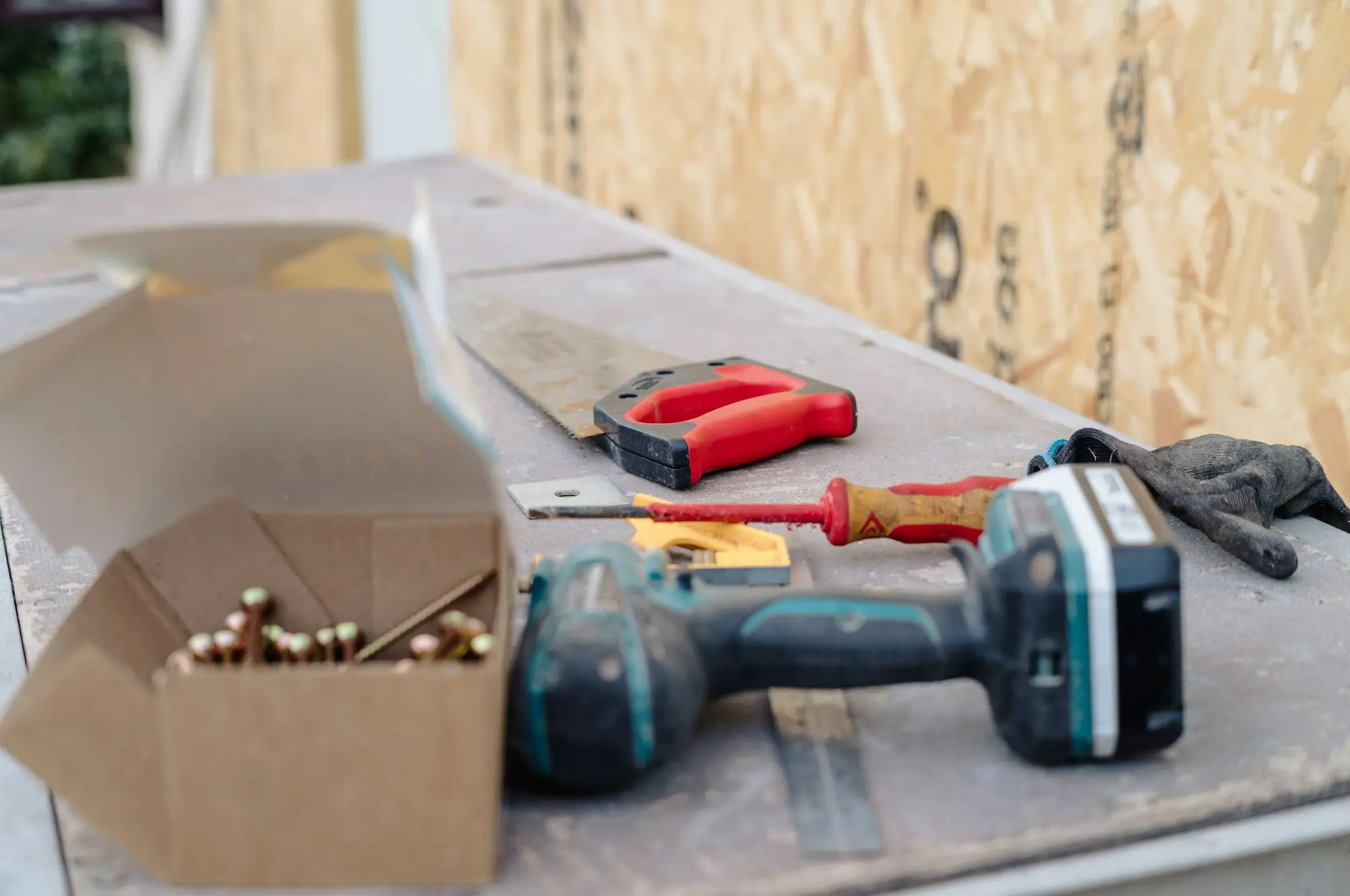 Tradie's drill, fixings and tools laid out on a job site bench